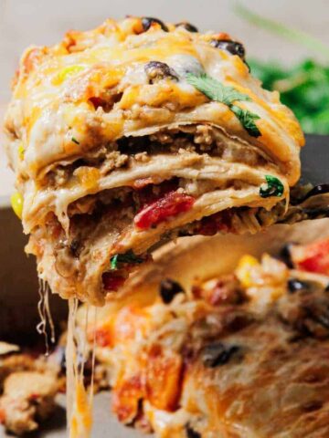 A cheesy slice of layered Mexican casserole being lifted from a baking dish, with melted cheese stretching.