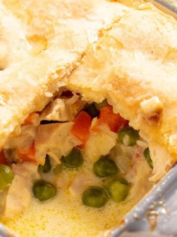 A baked pot pie with a golden crust, showing peas, carrots, and chicken filling inside.