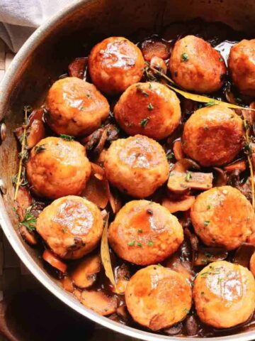 A skillet of glazed meatballs in sauce with mushrooms and herbs, viewed from above.