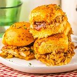 Three Slow Cooker Cranberry BBQ Turkey Sliders stacked on a white plate, featuring golden buns and juicy, shredded turkey filling.