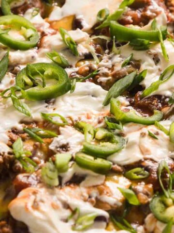 A close-up of loaded nachos topped with ground beef, beans, cheese, sour cream, jalapeños, and green onions.
