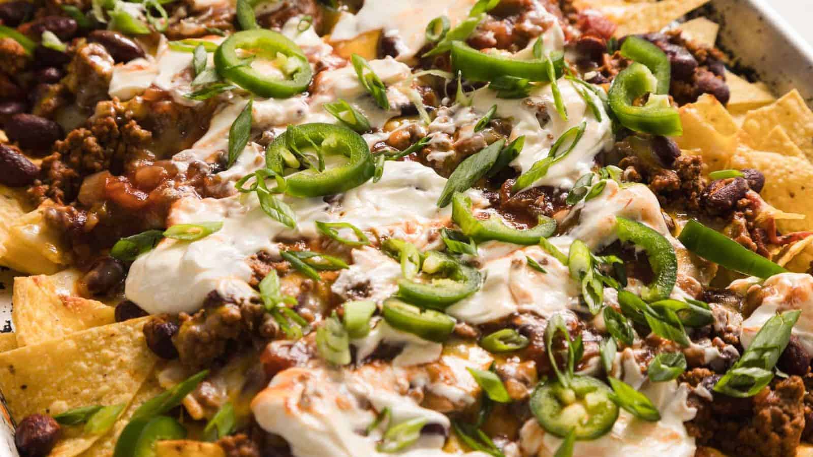 A close-up of loaded nachos topped with ground beef, beans, cheese, sour cream, jalape&ntilde;os, and green onions.