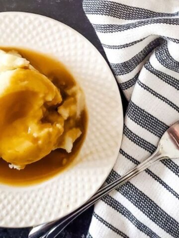 A plate of mashed potatoes smothered with Guinness Gravy on a white plate.