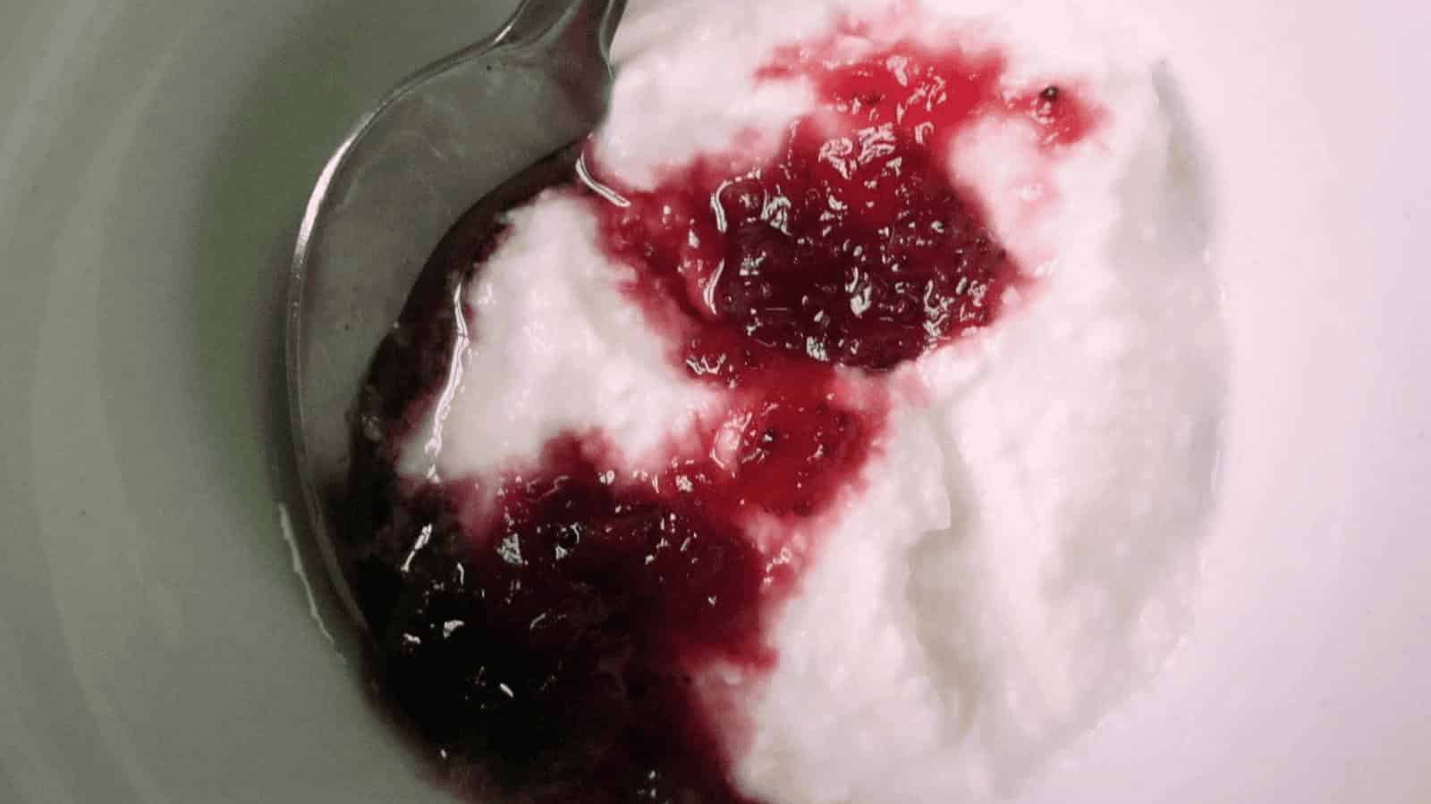 A spoonful of yogurt topped with red berry jam in a white bowl.