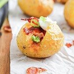 Loaded Baked Potato Bites topped with bacon, sour cream, and chopped green onions on parchment paper.