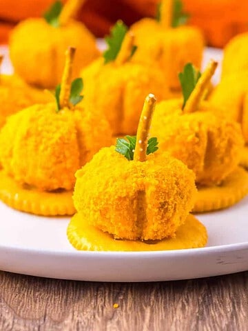 Mini pumpkin-shaped cheese balls on crackers with pretzel stems.