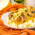 Plate of mashed potatoes topped with creamy mushroom gravy and slow cooker Olive Garden Chicken Marsala, garnished with fresh herbs.