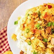 A plate of cheesy Neiman Marcus Chicken casserole with green onions and almonds, served over mashed potatoes, with crackers on the side.