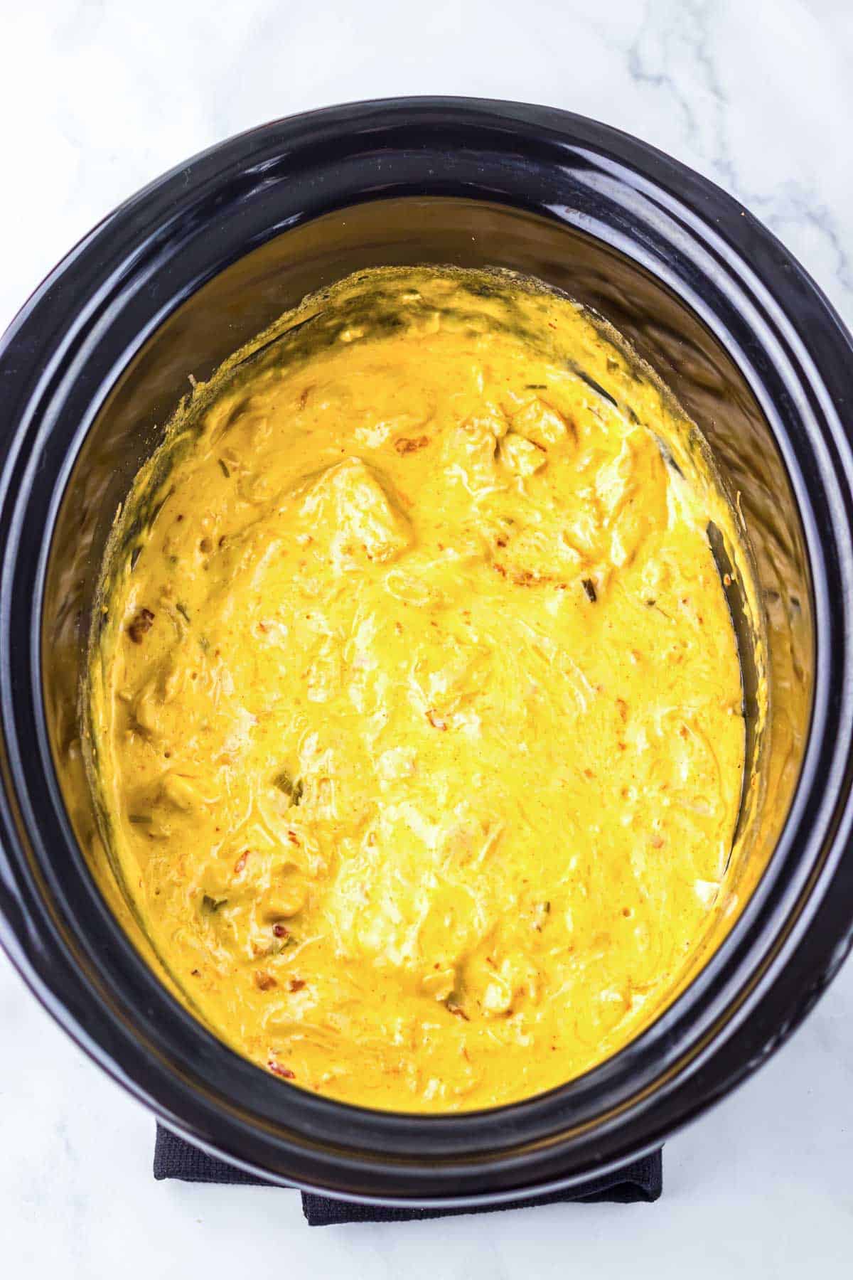 A slow cooker filled with creamy, yellow cheese dip sits on a white marble surface&mdash;perfect for pairing with your favorite chicken recipe.