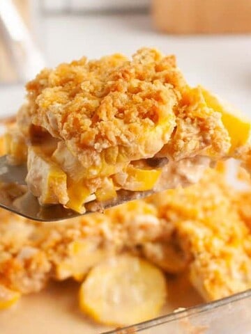 A serving of squash casserole is lifted from a baking dish with a spoon.