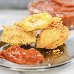 Two pieces of toasted ravioli with marinara sauce on a plate, one cut open to reveal the filling. Try this appetizer as an easy air fryer recipe for crunchy, delicious results.
