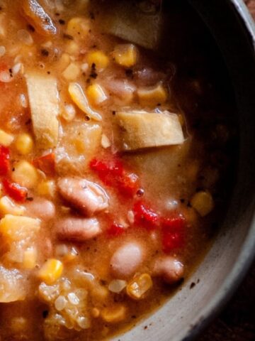 A bowl of hearty vegetable soup with beans, corn, potatoes, and red peppers.