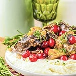 Slow cooker cranberry short ribs with gravy, cranberries, and herbs served over mashed potatoes on a white plate.
