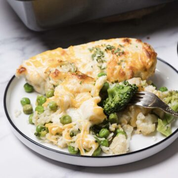 A fork rests on a plate of cheesy vegetable casserole with broccoli, peas, and rice&mdash;an easy casserole recipe perfect for using minute rice.