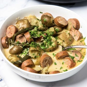A bowl of creamy soup featuring Swamp Potatoes, tender green beans, chopped herbs, and sliced smoked sausage&mdash;perfectly simmered in a slow cooker for rich, comforting flavor.