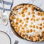 Baked sweet potato casserole with toasted marshmallows on top, next to a serving utensil, plate, and fork.