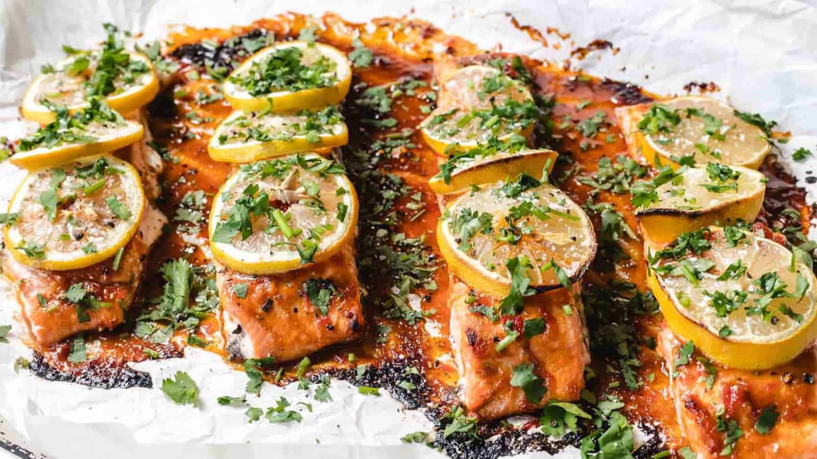 Baked salmon fillets topped with lemon slices and fresh herbs on a sheet of parchment paper.