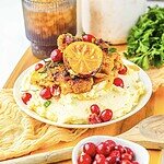 Roasted Cranberry Chicken with lemon sits atop mashed potatoes, garnished with herbs on a white plate.