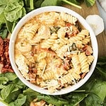 A bowl of creamy rotini pasta with spinach, sun-dried tomatoes, and cheese, inspired by the flavors of Marry Me Chicken, surrounded by fresh spinach leaves.
