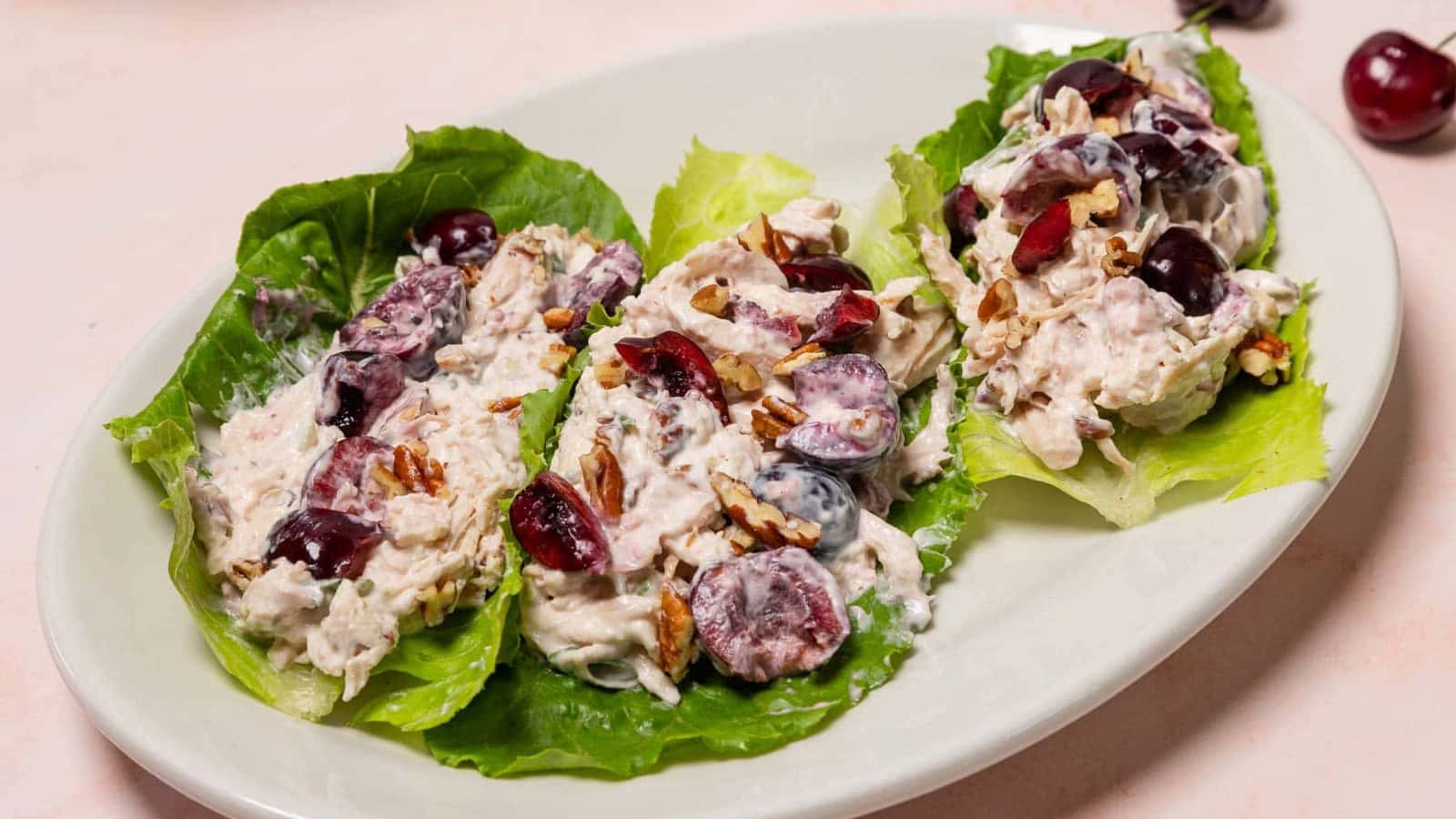 Three lettuce leaves topped with chicken salad, grapes, and pecans on a white oval plate.