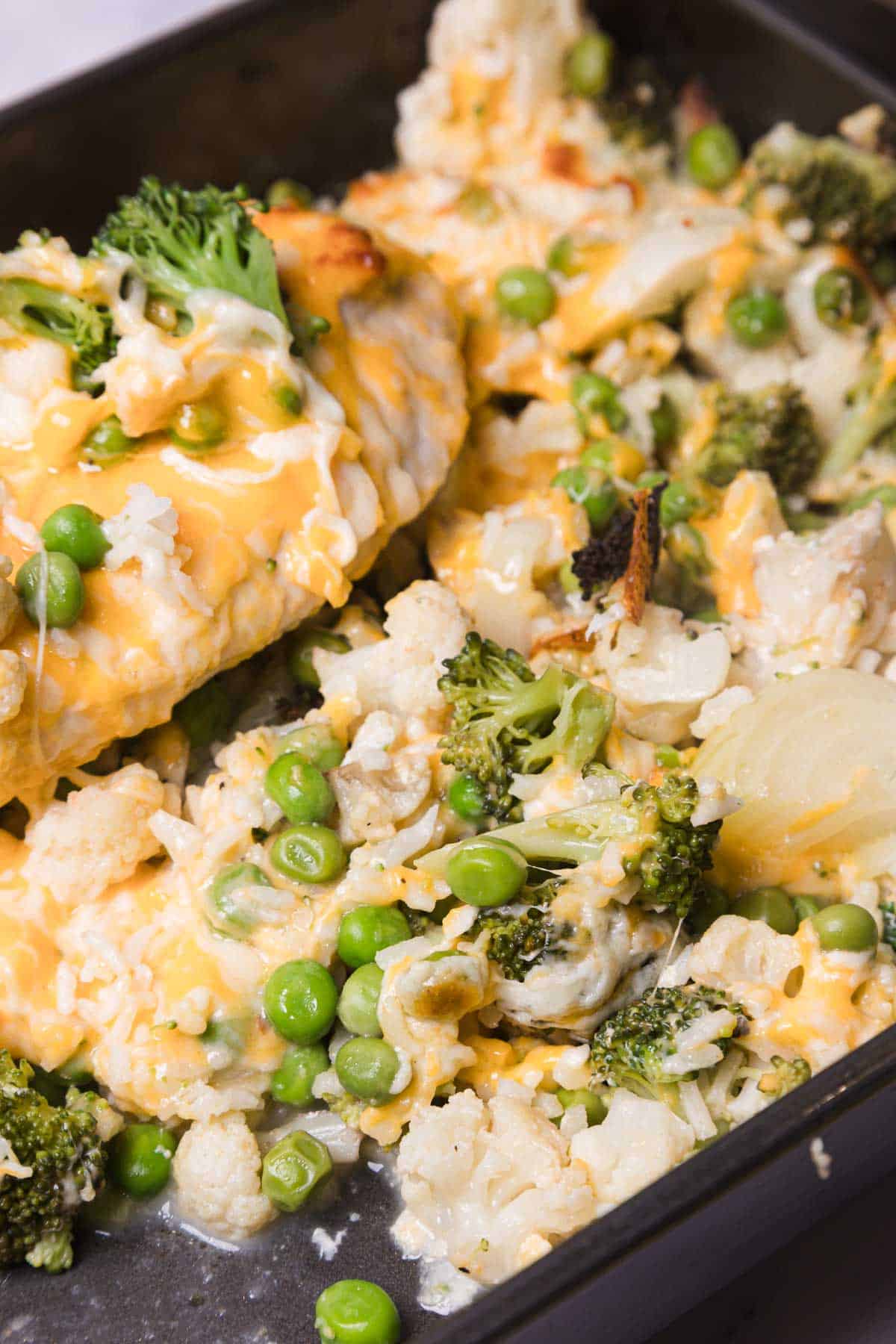 Closeup of baked vegetables, including broccoli, cauliflower, peas, and cheese, in a dark roasting pan&mdash;perfect as a side for your favorite Chicken and Rice Casserole.