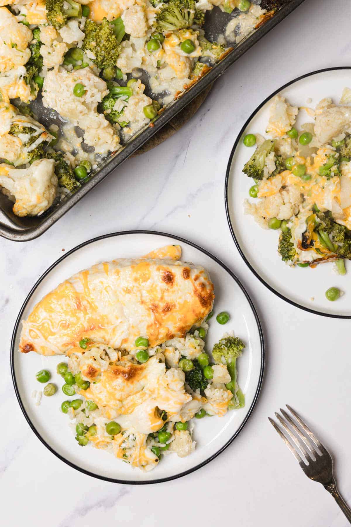 Baked cheesy chicken with broccoli, cauliflower, peas, and Minute Rice makes a delicious chicken and rice casserole recipe served on two white plates next to a baking tray.