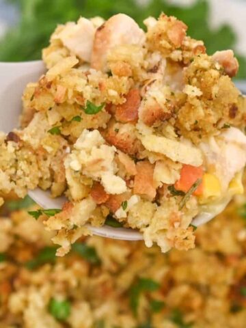 A spoonful of chicken and stuffing casserole held above a pan filled with the same casserole.