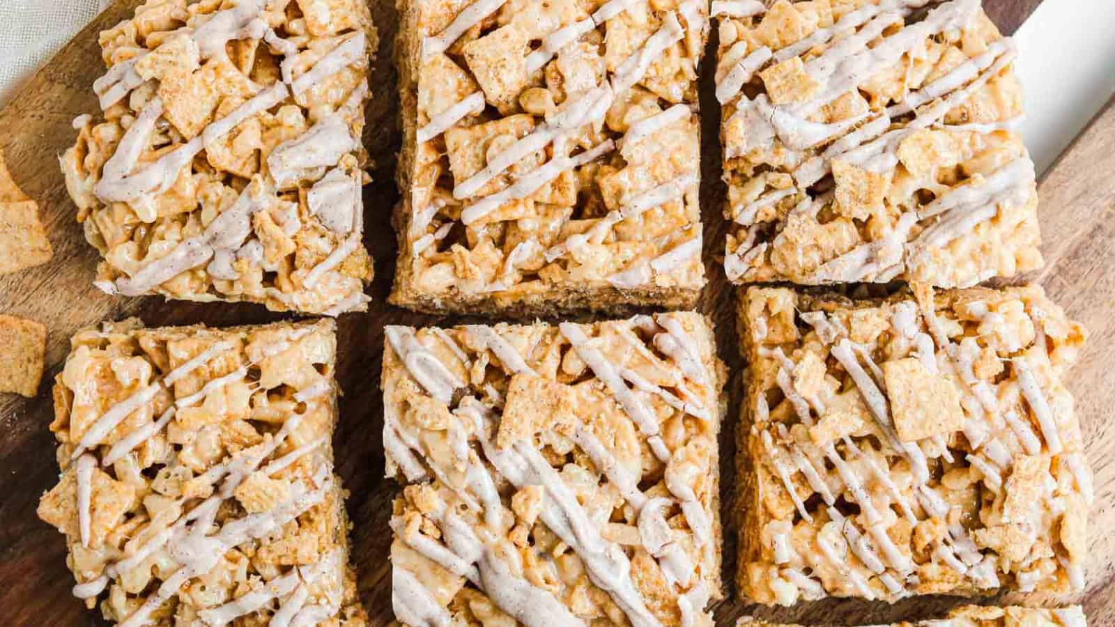 Six cinnamon cereal bars drizzled with white icing, arranged on a wooden surface.