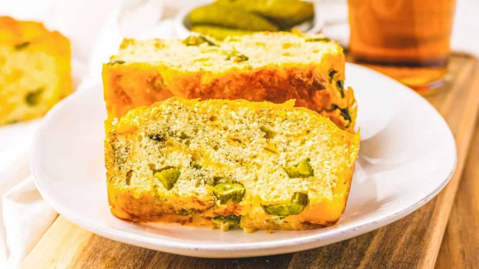 Two slices of savory bread with green pieces on a white plate, served on a wooden board.