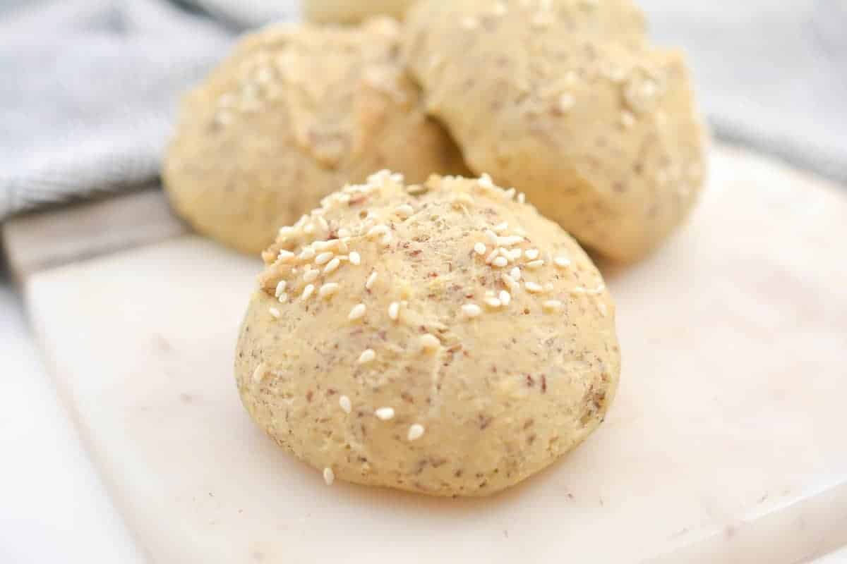 Close-up of round bread rolls topped with sesame seeds on a white cutting board.