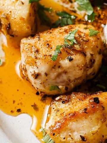 Succulent seasoned chicken breasts with herbs and spices, served with a flavorful sauce on a white plate.