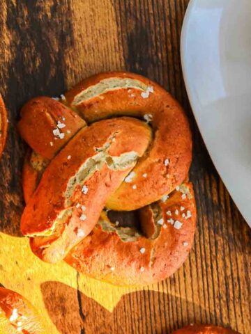 Soft pretzels with coarse salt on a wooden surface, with mustard dipping sauce on a white plate.