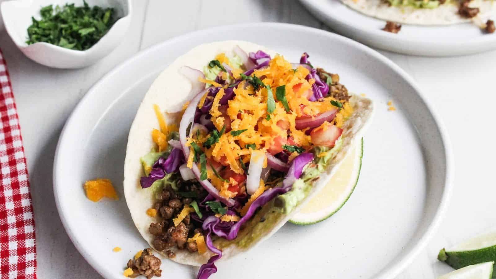 Two pork tacos on a white plate with lime wedges.