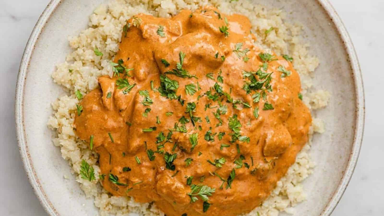 Bowl of instant pot butter chicken atop cauliflower rice in a bowl.