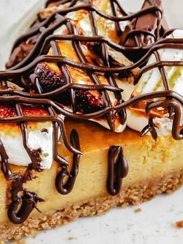 A slice of pie topped with toasted marshmallows and drizzled with chocolate sauce on a white plate.