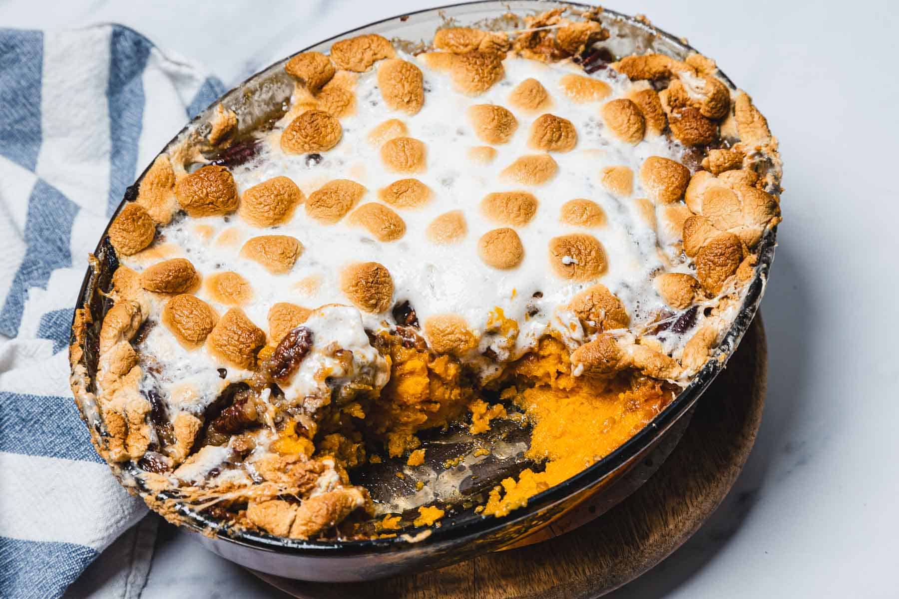 A classic Sweet Potato Casserole topped with golden, toasted marshmallows, with a warm serving scooped out to reveal the creamy filling.