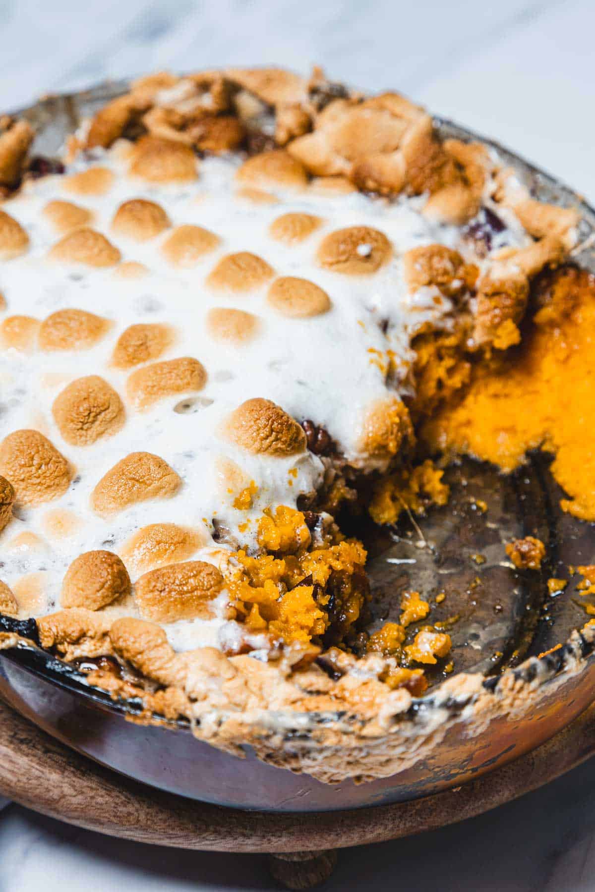 A sweet potato casserole with marshmallows, topped with perfectly toasted marshmallows and a serving spooned out.