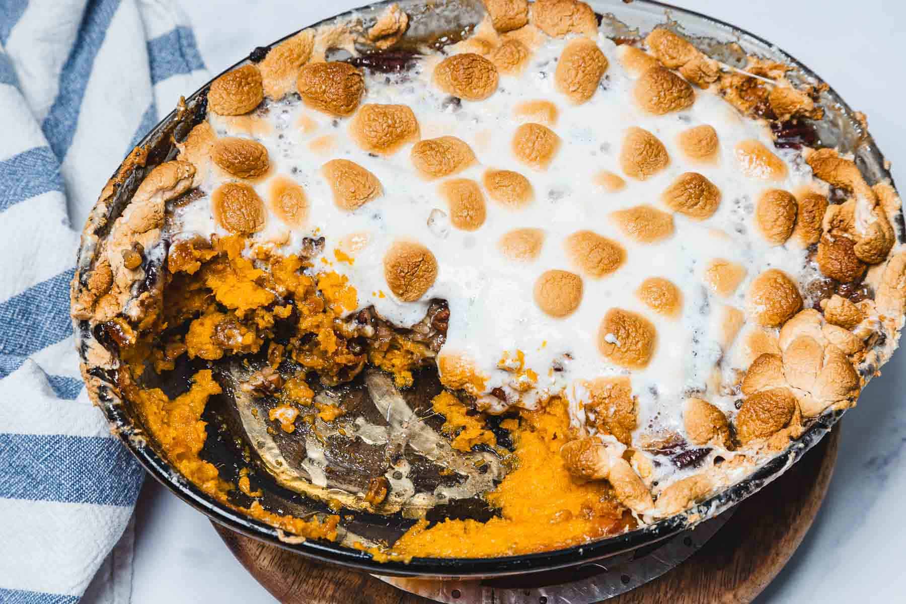 Casserole dish of sweet potato casserole with marshmallows, topped with toasted marshmallows and a portion scooped out.