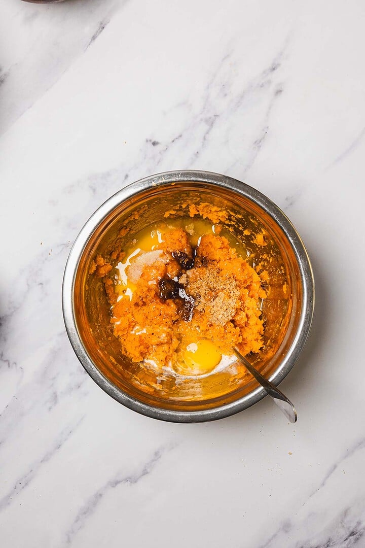 A metal bowl with mashed sweet potatoes, eggs, and spices on a marble countertop—perfect for starting your Sweet Potato Casserole With Marshmallows.