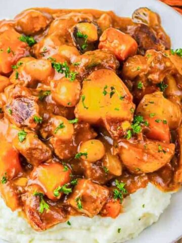 Beef stew with carrots and potatoes served over mashed potatoes, garnished with chopped parsley.