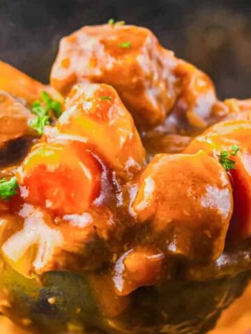 A ladle of hearty beef stew with carrots, potatoes, and parsley garnish, shown close up.