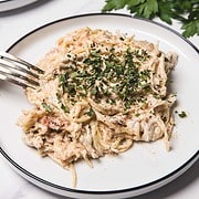 A plate of creamy slow cooker chicken spaghetti garnished with chopped herbs, with a fork and fresh parsley on the side.