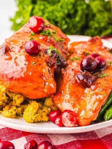 Plate of glazed chicken with cranberries, green beans, and stuffing on a red and white checkered cloth.