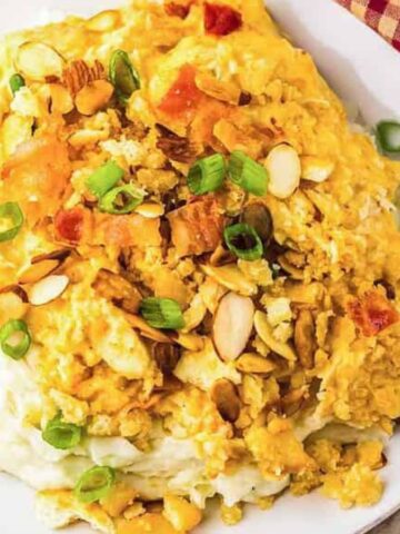 A plate of cheesy chicken casserole topped with sliced almonds and green onions on mashed potatoes.