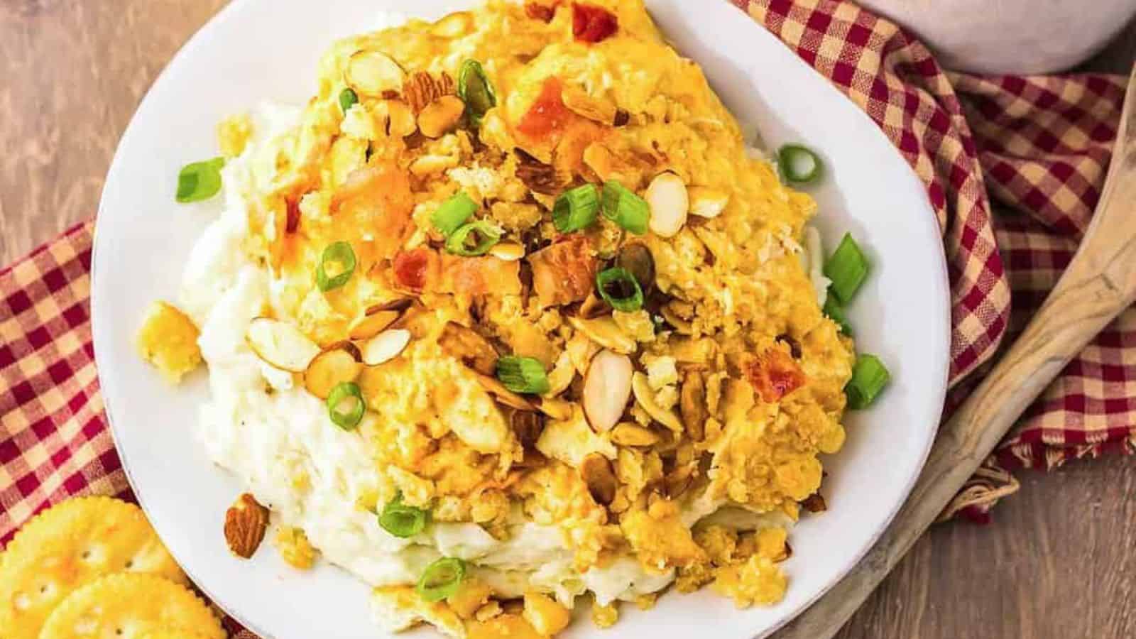 A plate of cheesy chicken casserole topped with sliced almonds and green onions on mashed potatoes.