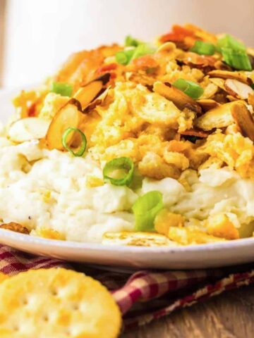 A plate of creamy casserole topped with sliced almonds and green onions, served with round crackers.