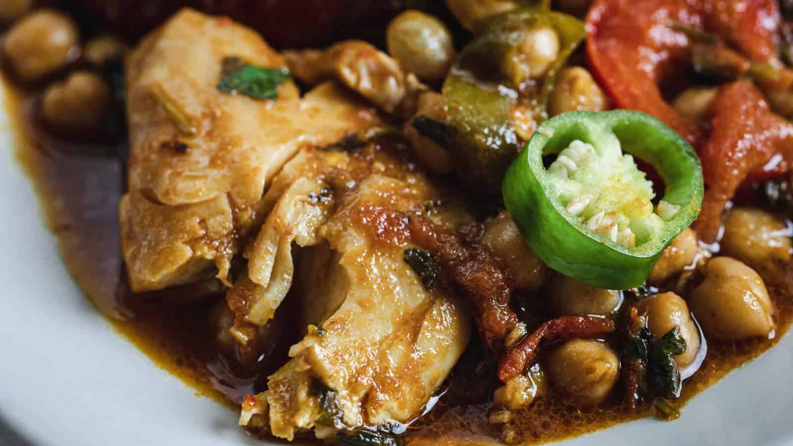 A cooked fish with chickpeas, tomatoes, green pepper, and herbs in a savory sauce.