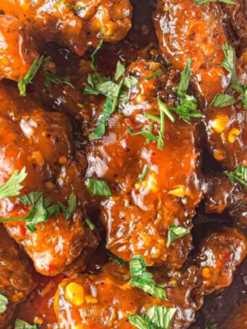 Close-up of saucy chicken wings garnished with chopped cilantro in a bowl.