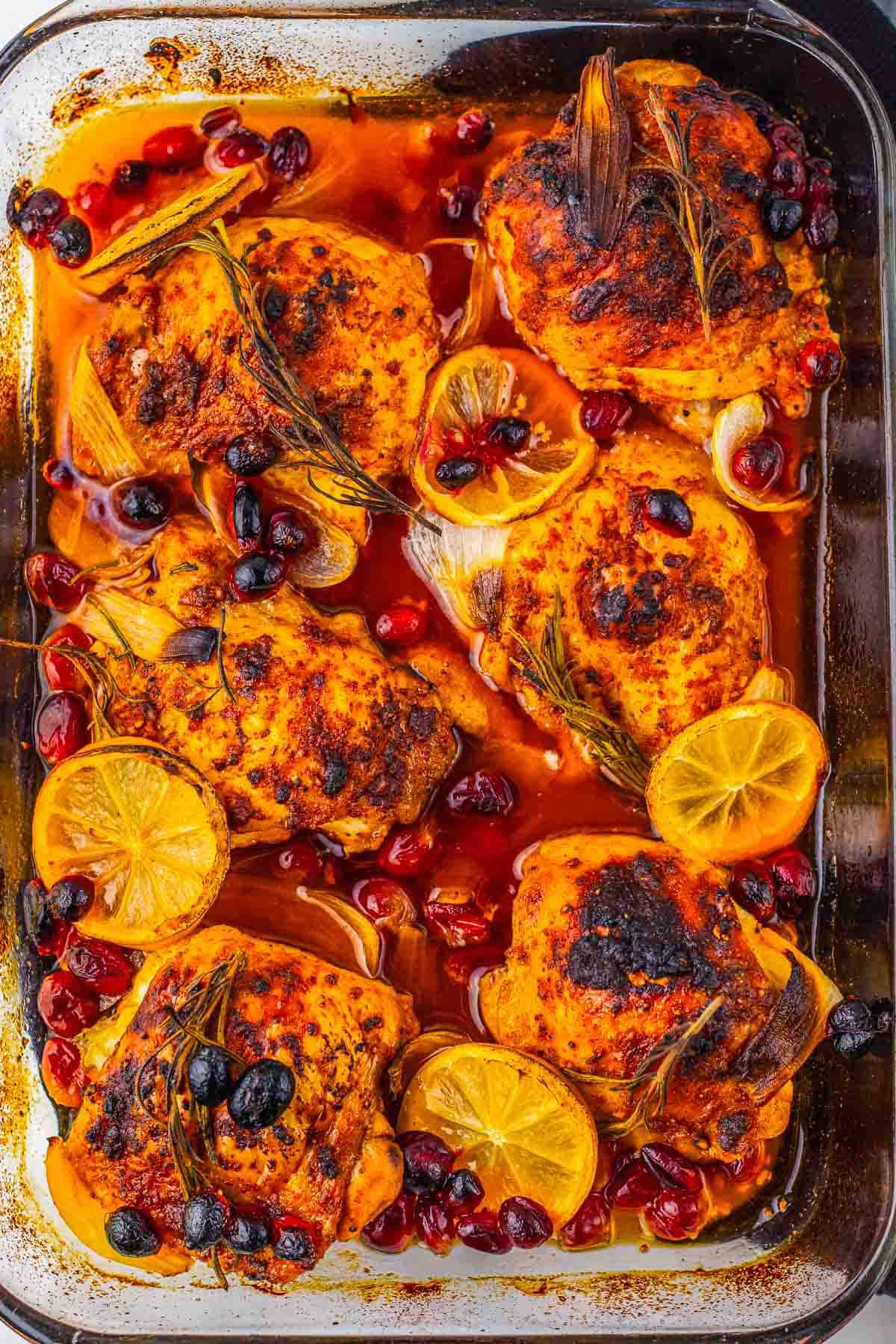 Roasted Cranberry Chicken Thighs baked with lemon slices, cranberries, and herbs in a glass baking dish.