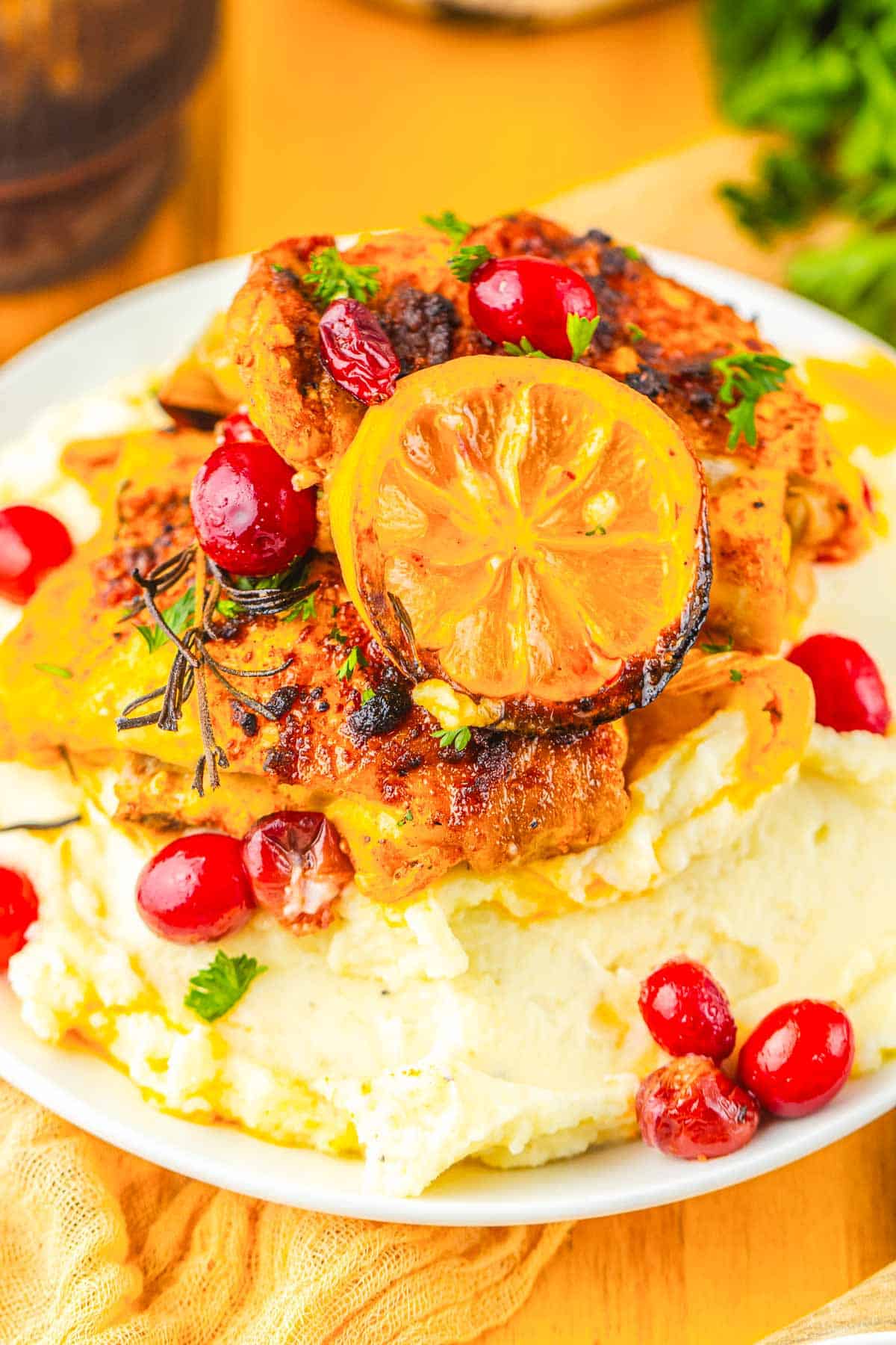 Enjoy Roasted Cranberry Chicken featuring grilled chicken thighs with roasted lemon, cranberries, and herbs on creamy mashed potatoes, served on a white plate.